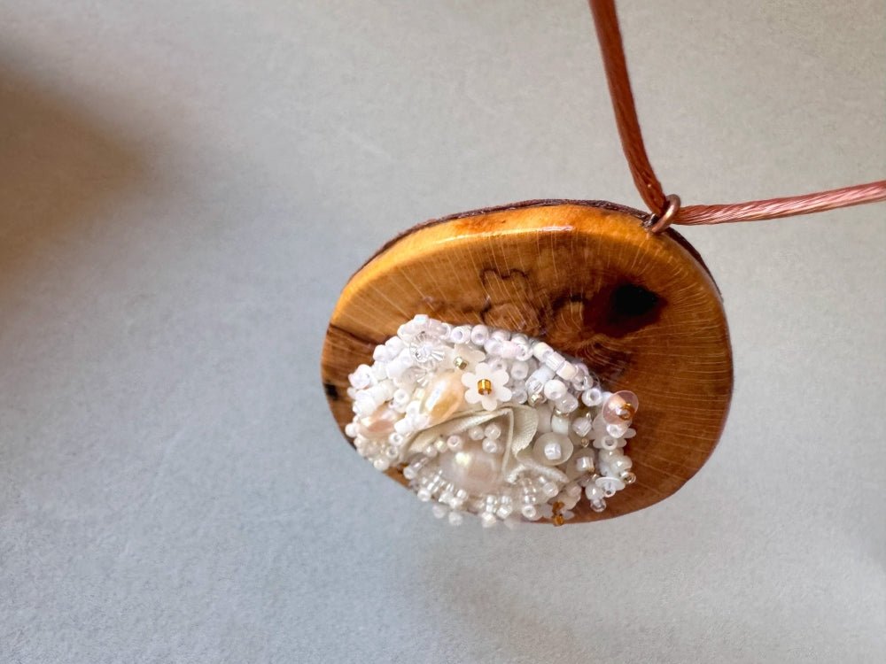 Exclusive wooden pendant with textile and beaded floral center crafted in various hues of white