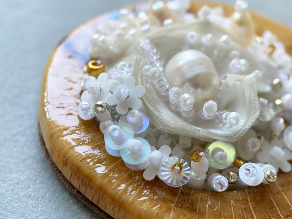 Exclusive wooden pendant with textile and beaded floral center crafted in various hues of white