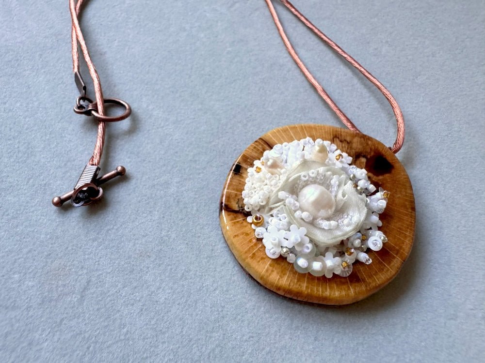 Exclusive wooden pendant with textile and beaded floral center crafted in various hues of white