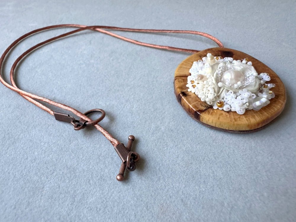Exclusive wooden pendant with textile and beaded floral center crafted in various hues of white