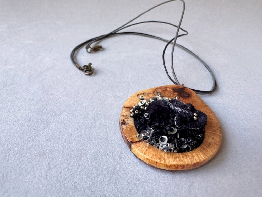 Exclusive wooden pendant with textile and volume-beaded floral inlay crafted in elegant black