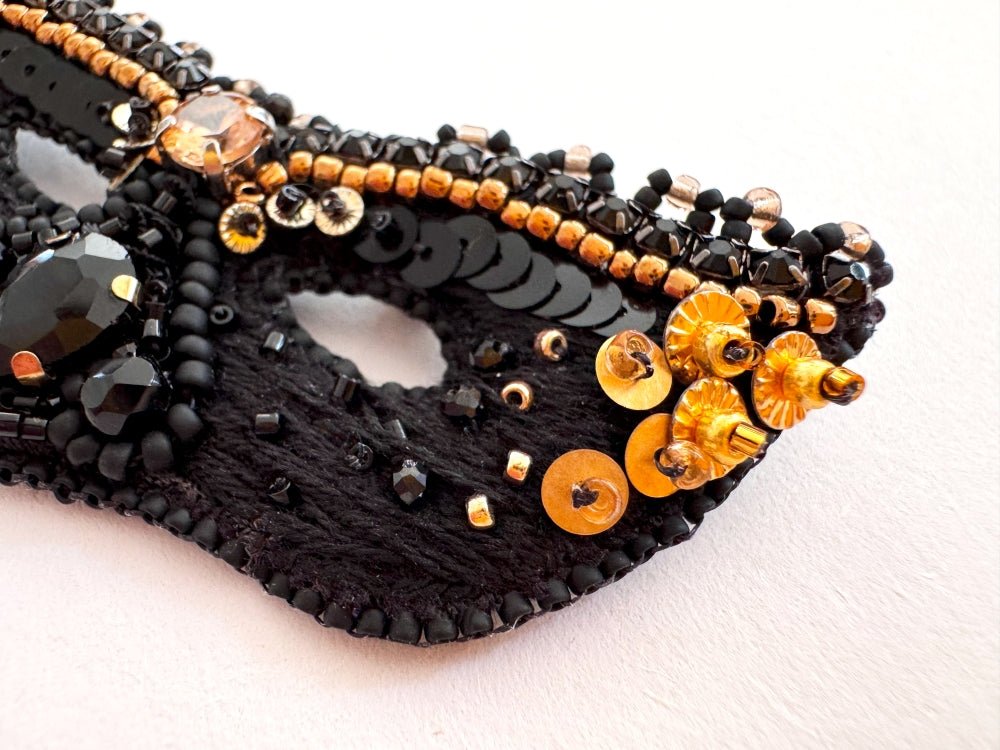 Handmade brooch in the shape of a Venetian masquerade mask crafted in black and gold from beads, sequins, rhinestones and embroidery - Ornamentico Shop