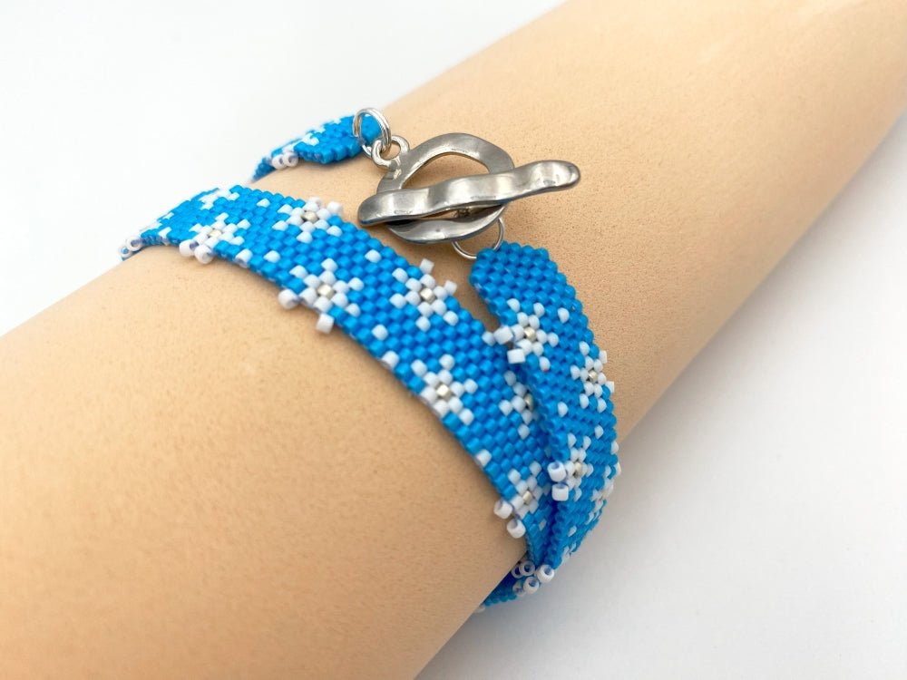 Handmade beaded bracelet featuring white snowflakes on a bright azure blue - Ornamentico shop