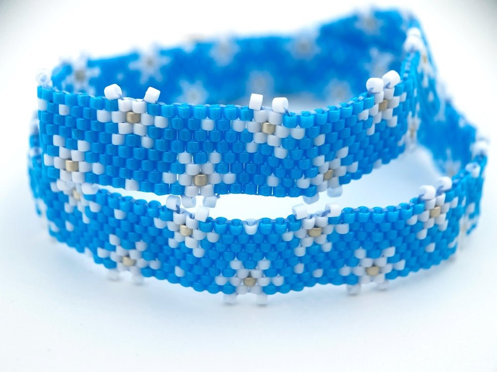 Handmade beaded bracelet featuring white snowflakes on a bright azure blue - Ornamentico shop