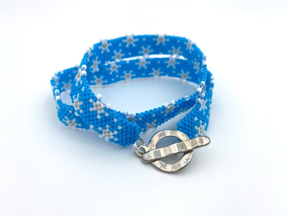 Handmade beaded bracelet featuring white snowflakes on a bright azure blue - Ornamentico shop