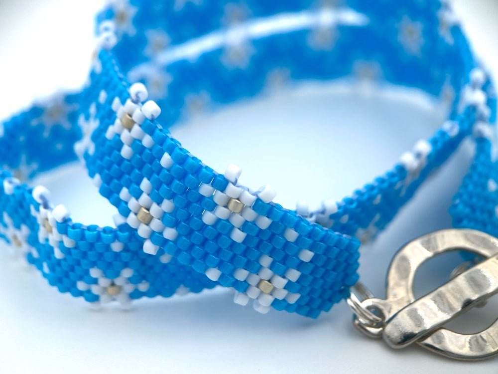 Handmade beaded bracelet featuring white snowflakes on a bright azure blue - Ornamentico shop