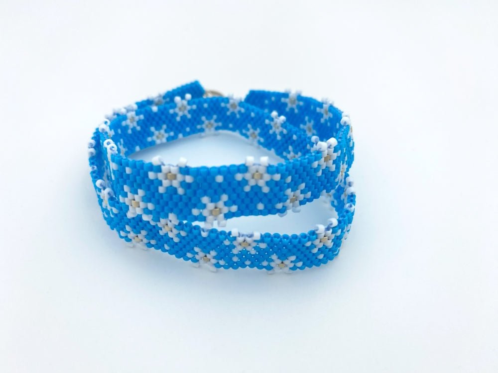 Handmade beaded bracelet featuring white snowflakes on a bright azure blue - Ornamentico shop