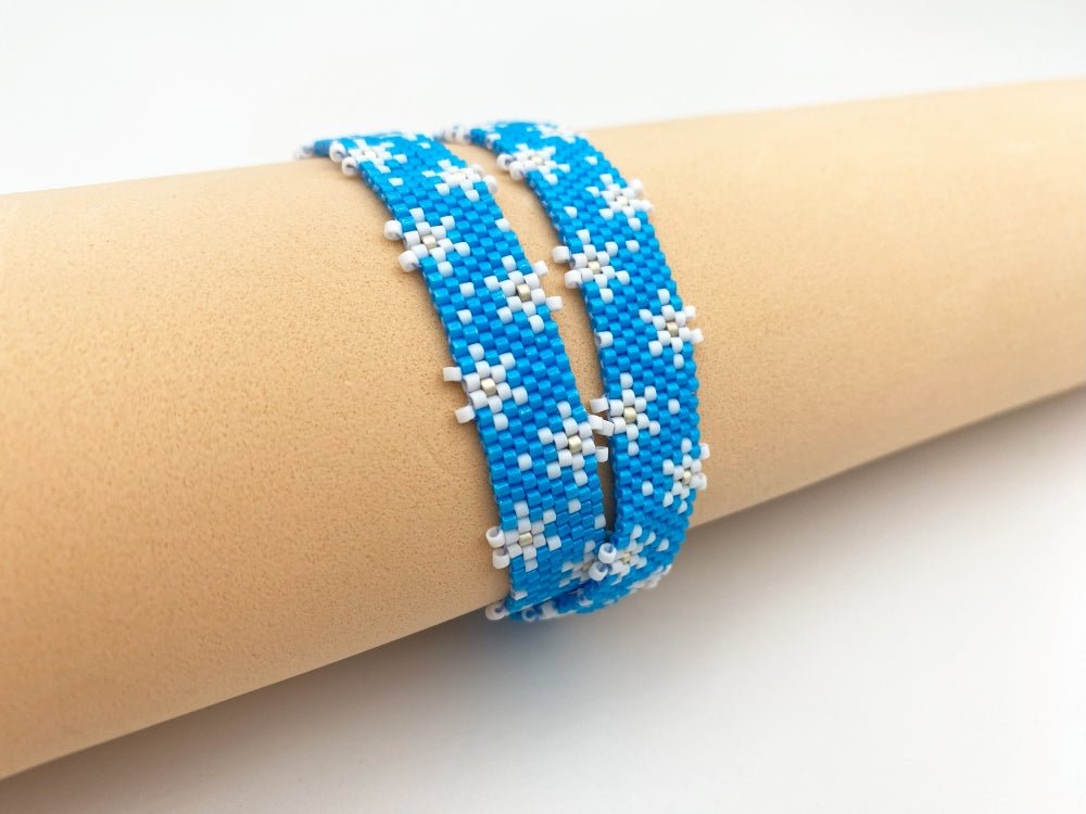 Handmade beaded bracelet featuring white snowflakes on a bright azure blue - Ornamentico shop