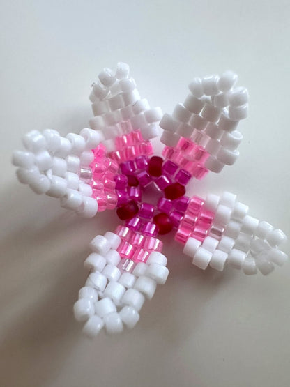 A handmade beaded cherry blossom ornament featuring white outer arms, pink middle sections, and a dark red center, crafted from Miyuki  beads on a plain light background.