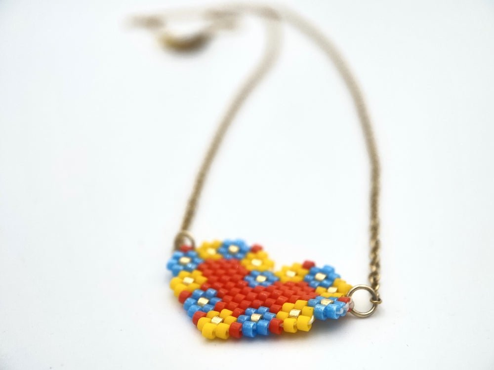 Heart-shaped pendant made from Miyuki Delica beads in bright red, yellow, blue and gold colors using peyote stitch technique