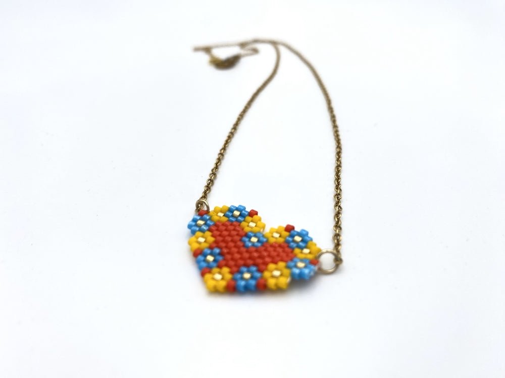 Heart-shaped pendant made from Miyuki Delica beads in bright red, yellow, blue and gold colors using peyote stitch technique