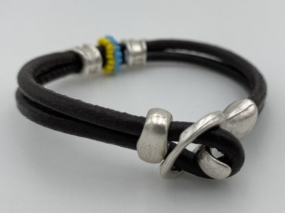 Handmade men's bracelet from leather decorated with two large helmet beads and insert from color beads. Beaded insert is made in Ukrainian flag colors - Ornamentico shop