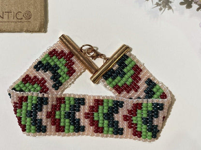 Handmade bracelet made from beads crafted in weaved technique. Geometric green, white and red festive pallet.