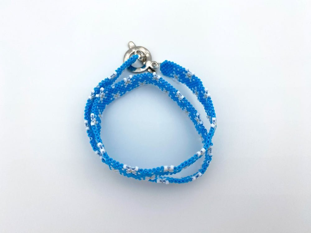 Handmade beaded bracelet featuring white snowflakes on a bright azure blue - Ornamentico shop