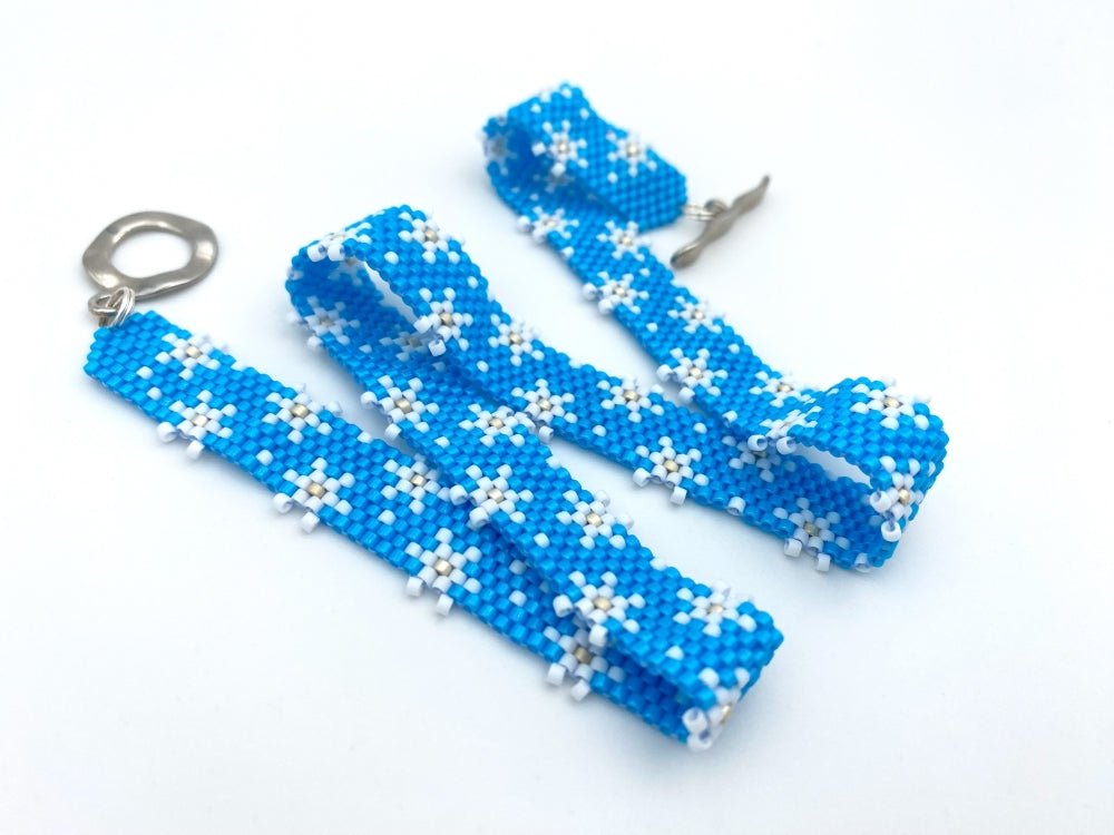 Handmade beaded bracelet featuring white snowflakes on a bright azure blue - Ornamentico shop